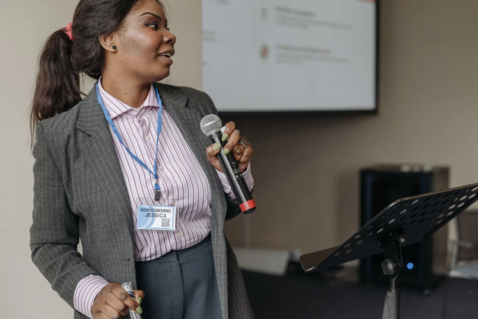 Mulher apresentando numa reunião, com microfone, falando com confiança