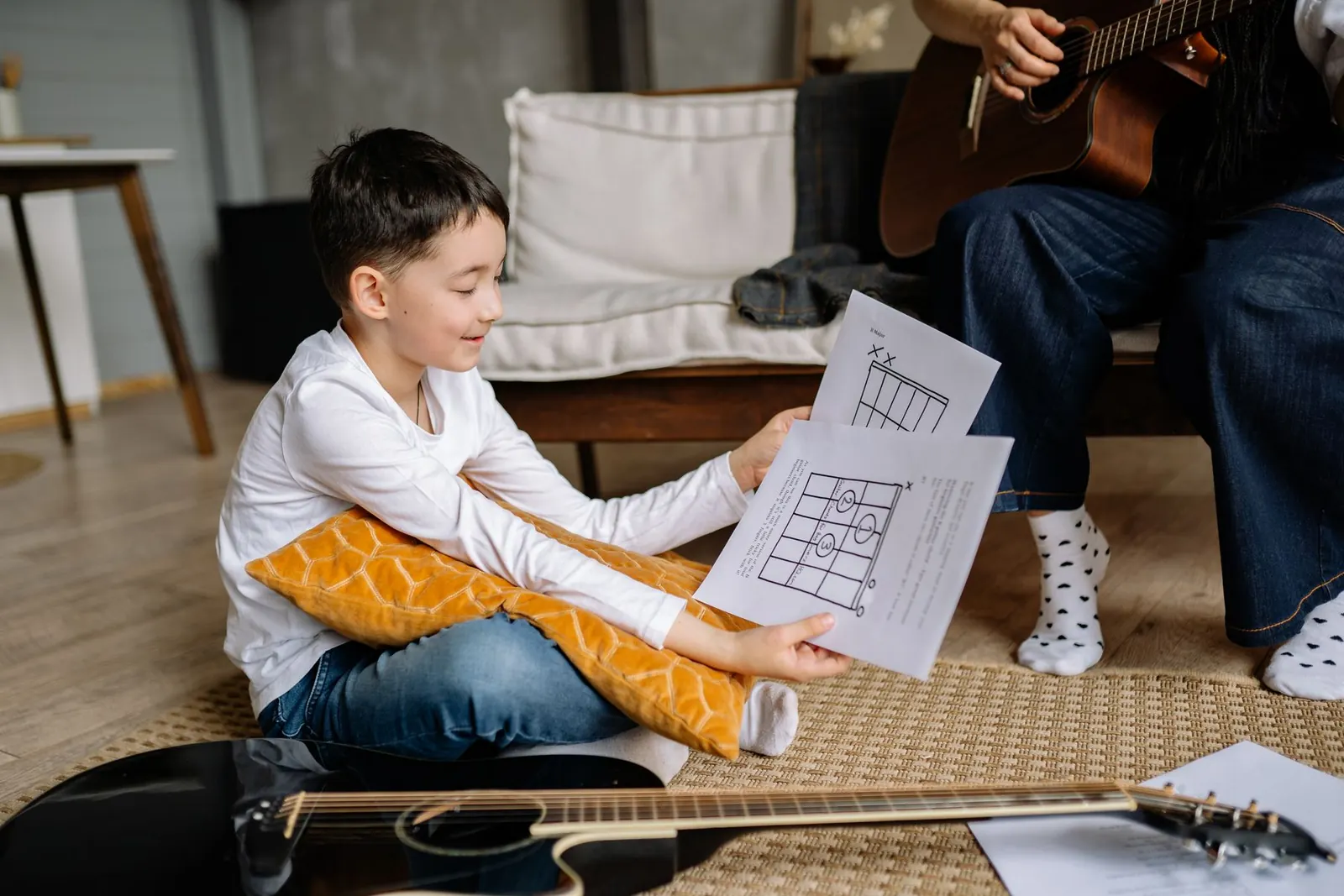 Criança olhando um diagrama de acordes, com o violão no chão