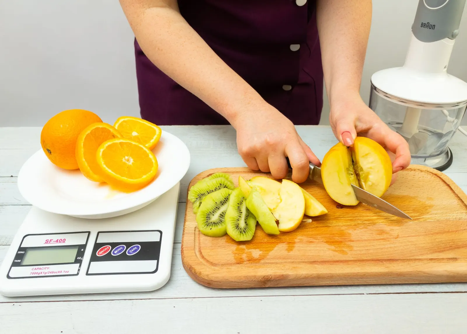 Mãos cortando frutas ao lado de uma balança de cozinha