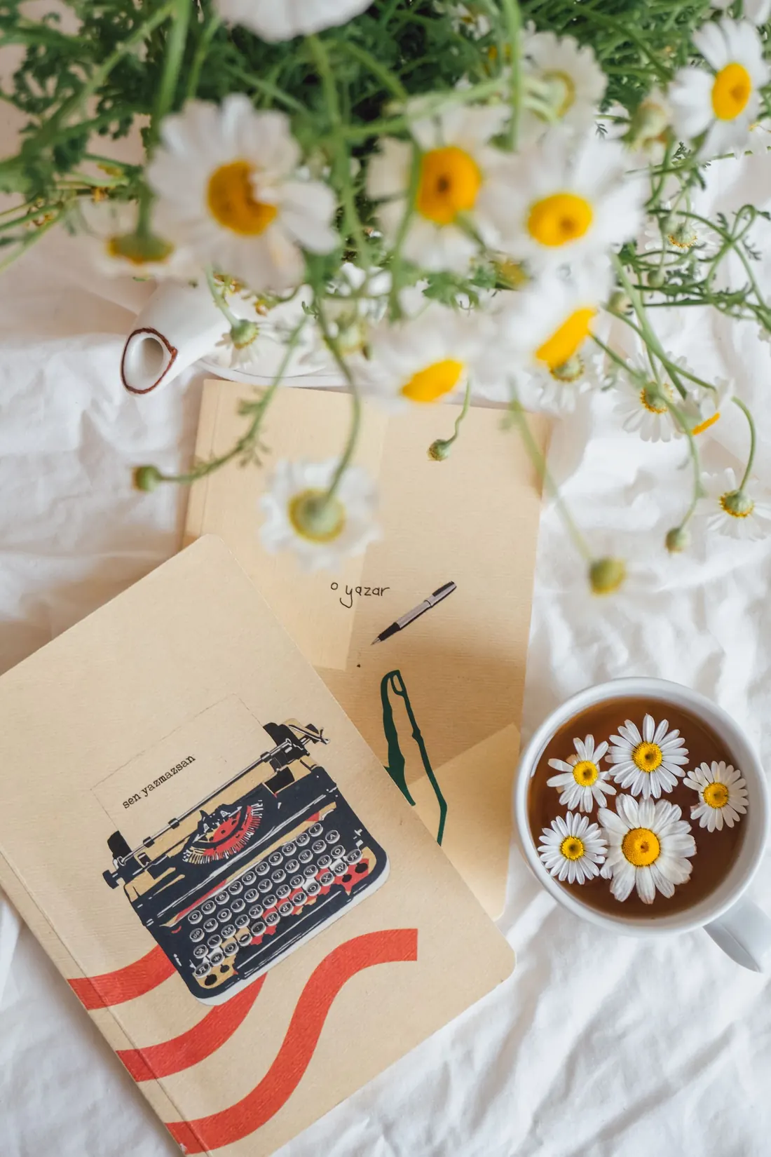 Margaridas, caderno e chá de camomila sobre lençol branco