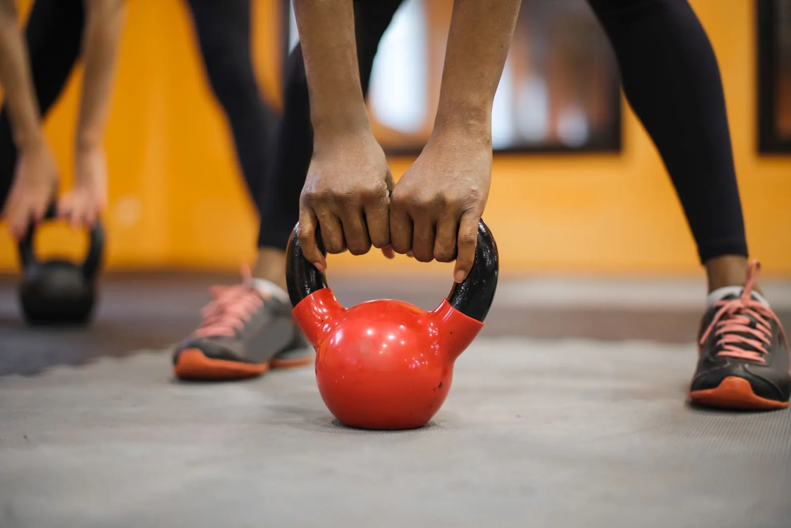 Mãos segurando um kettlebell vermelho no chão