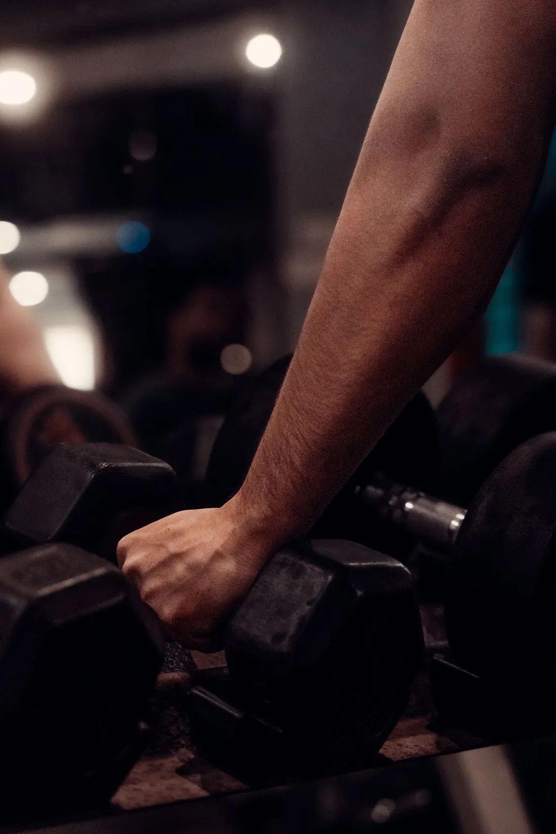 Braço pegando um halter na academia, tons escuros